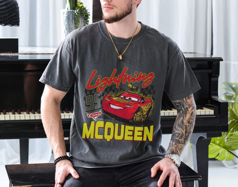 Puede incluir: Camiseta gris oscuro con un dise&ntilde;o de Rayo McQueen de la pel&iacute;cula Cars. El dise&ntilde;o incluye el texto "Lightning McQueen" en rojo y amarillo, con el n&uacute;mero "95" y la palabra "Cars".