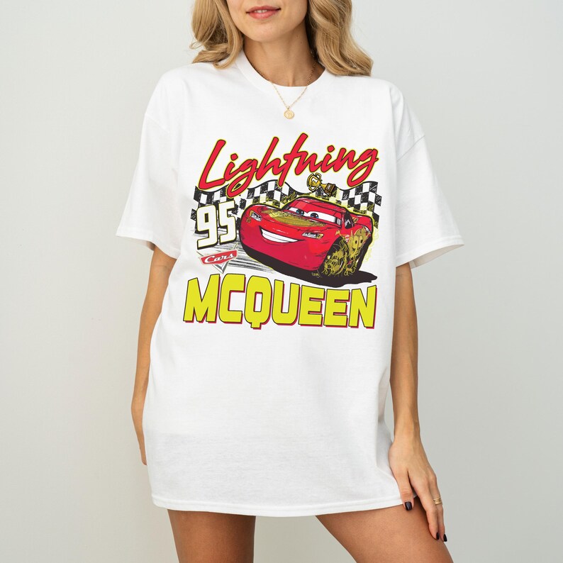 Puede incluir: Camiseta blanca con un gr&aacute;fico de Rayo McQueen de la pel&iacute;cula Cars. El dise&ntilde;o incluye el texto "Lightning McQueen 95" en rojo y amarillo, con un fondo de bandera a cuadros. La camiseta tiene un corte casual y oversize.