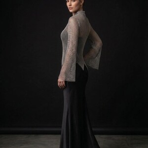 May include: A long-sleeved top made of silver-toned metallic chainmail with a high neckline and flared cuffs, paired with a floor-length black skirt. The chainmail garment features a repeating interlocking ring pattern and a pointed hemline.
