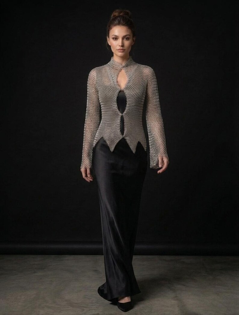 May include: A long-sleeved silver chainmail top featuring a high collar and a front cutout design, layered over a floor-length black satin dress. The metallic mesh garment has a pointed hemline and long sleeves, providing a structured contrast to the smooth, flowing black fabric of the full-length dress underneath.