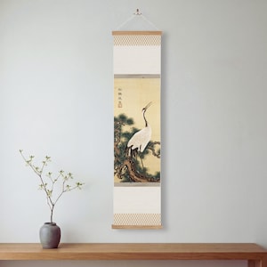 May include: A vertical wall hanging scroll featuring a painting of a white crane with a red crown standing on a dark pine branch. The artwork includes black calligraphy and a red seal. The scroll has a cream-colored border with a geometric pattern.