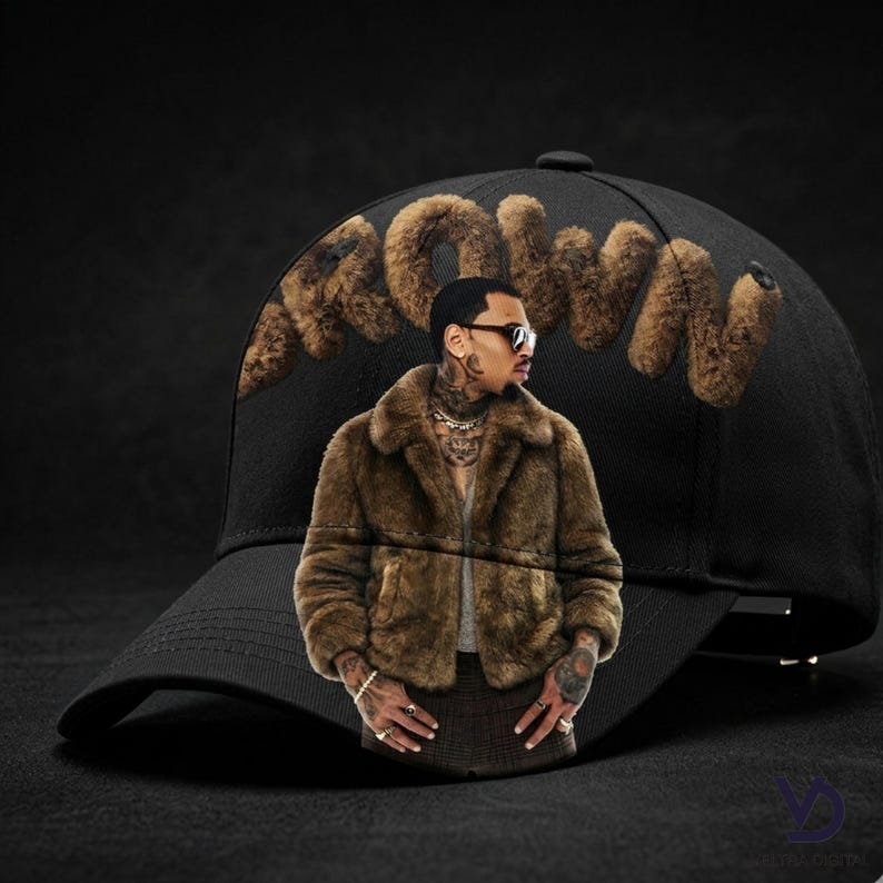 Puede incluir: Gorra de b&eacute;isbol negra con la palabra "BROWN" en letras de piel sint&eacute;tica marr&oacute;n. La gorra presenta una imagen de una persona que lleva un abrigo de piel marr&oacute;n y gafas de sol. La gorra tiene una visera curva.