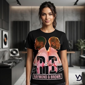 Puede incluir: Camiseta negra con un gr&aacute;fico de dos hombres con trajes rosas, con el texto "THE RB TOUR" y "RAYMOND & BROWN". El dise&ntilde;o incluye firmas y un logotipo. La camiseta la lleva una persona.