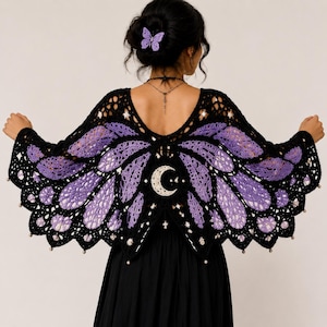 May include: A black and purple crochet shawl shaped like butterfly wings, featuring a central white crescent moon motif and small white beads along the scalloped edges. The garment is worn over a plain black top, with a matching purple butterfly hair clip.