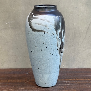 May include: A tall, gray ceramic vase with black and white abstract designs. The vase has a speckled glaze and a rounded bottom.