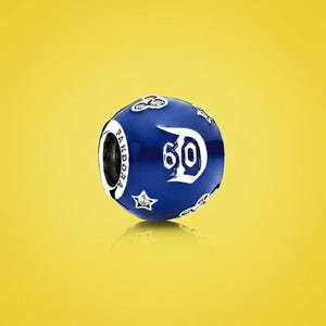 Puede incluir: Un charm Pandora azul y blanco con el número "60" en una fuente estilizada. El charm tiene forma esférica con estrellas y detalles de cabeza de Mickey Mouse. La palabra "Pandora" es visible en el lateral.