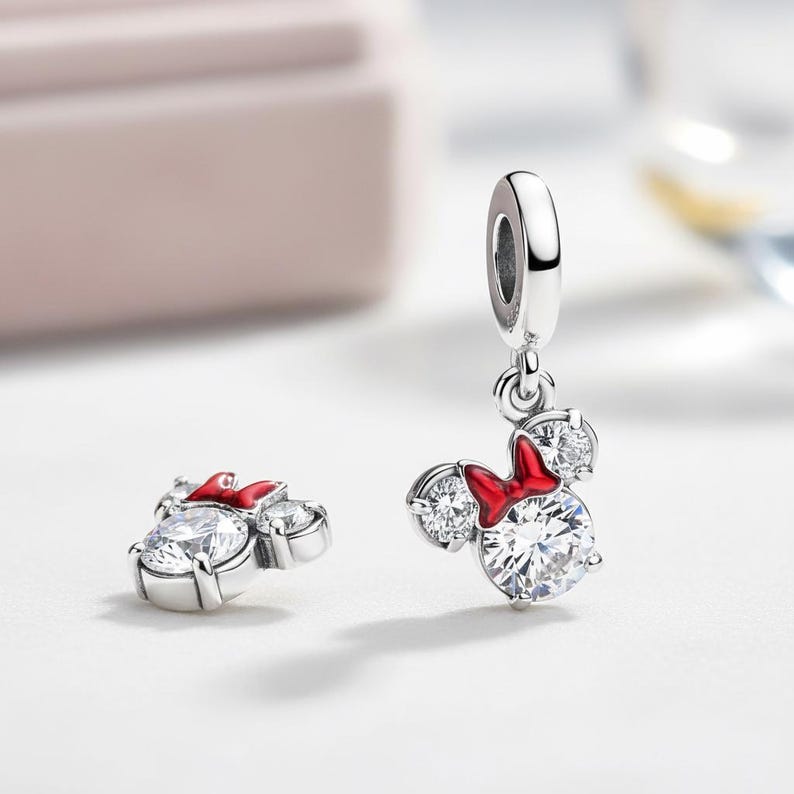 Peut inclure: Deux breloques en argent avec un design de Minnie Mouse. Chaque breloque a une grosse pierre de zircone cubique transparente pour le visage, deux petites pierres pour les oreilles et un n&oelig;ud rouge. Une breloque est suspendue, l'autre est &agrave; plat.