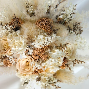 K&ouml;nnte beinhalten: Nahaufnahme eines Trockenblumenstrau&szlig;es mit cremefarbenen Rosen, Pampasgras und kleinen wei&szlig;en Bl&uuml;ten. Der Strau&szlig; hat eine nat&uuml;rliche Farbpalette mit braunen und beigen Akzenten.