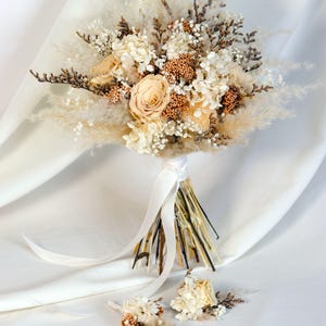 K&ouml;nnte beinhalten: Ein Brautstrau&szlig; und zwei Knopflochblumen mit Trockenblumen in Creme-, Beige- und Braunt&ouml;nen. Der Strau&szlig; enth&auml;lt Rosen, Hortensien und Pampasgras, gebunden mit einem wei&szlig;en Band. Die Knopflochblumen haben &auml;hnliche Blumenarrangements.