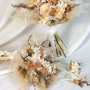 K&ouml;nnte beinhalten: Zwei Brautstr&auml;u&szlig;e und ein Knopfloch mit Trockenblumen. Die Str&auml;u&szlig;e haben eine Mischung aus beigem Pampasgras, wei&szlig;en und beigen Blumen und braunen Akzenten. Die Knopflochblume hat &auml;hnliche Elemente.