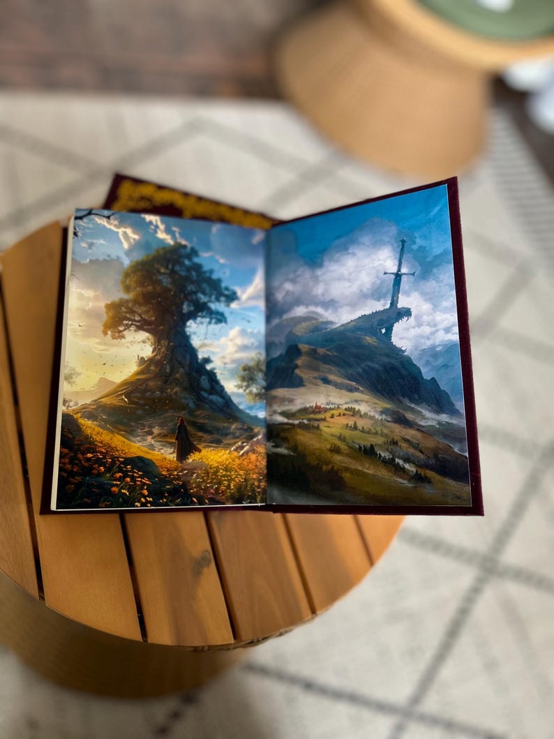 Pode incluir: Um livro aberto com duas ilustra&ccedil;&otilde;es de paisagens. Uma mostra uma grande &aacute;rvore numa colina, a outra uma montanha com uma espada. O livro tem uma capa bord&ocirc; e est&aacute; numa mesa de madeira.