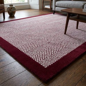 May include: A rectangular rug featuring a burgundy border and a cream and burgundy chevron design. The rug is laid on a wooden floor, with a coffee table and sofa visible in the background.