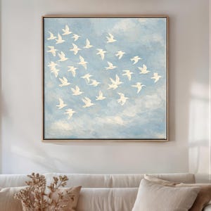 Framed canvas print of a flock of white birds in free flight against a soft powder-blue textured sky, painted in an oil-painting style with visible brushwork. Peaceful birds in flight wall art for nursery, bedroom, or minimalist living room décor — cream and sky blue palette, ready to hang.