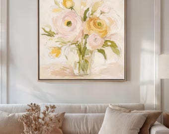 Puede incluir: Pintura floral enmarcada que presenta un ramo de flores amarillas y rosas en un jarrón de cristal transparente. La obra de arte tiene un estilo suave de acuarela con un fondo neutro y un marco marrón claro. La pintura se exhibe sobre un sofá color crema.