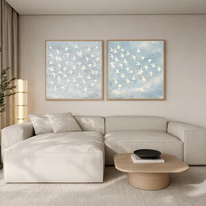 Two white bird canvas prints hung side by side above a neutral linen sofa, large framed diptych gallery wall in dusty blue and dove white, quiet luxury bird flock wall art set of 2 ready to hang
