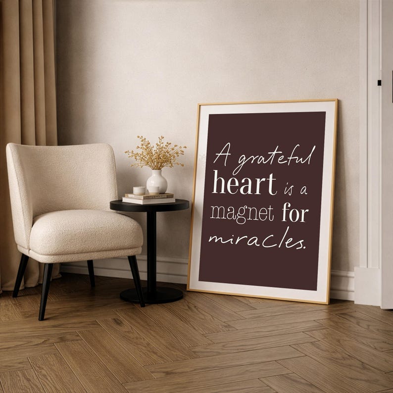 Pu&ograve; includere: Una stampa incorniciata con la scritta "A grateful heart is a magnet for miracles." La stampa &egrave; in una cornice dorata e appoggiata a un muro. Una sedia beige, un tavolino nero e un vaso con fiori secchi sono anche nella stanza.