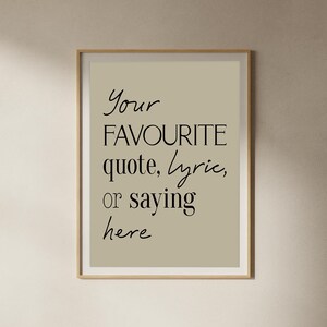 Pu&ograve; includere: Stampa incorniciata con il testo "Your FAVOURITE quote, lyric, or saying here" in corsivo nero. Lo sfondo &egrave; beige chiaro e la cornice &egrave; color legno chiaro.