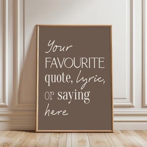 Pu&ograve; includere: Una stampa incorniciata con sfondo marrone e la scritta "Your FAVOURITE quote, lyric, or saying here" in bianco, con un carattere elegante. La cornice &egrave; di colore marrone chiaro e la stampa &egrave; esposta su una parete bianca e un pavimento in legno.