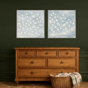 Large framed white birds in flight canvas — lighter sky with soft cloud tones and heart-shaped dove flock formation, impasto texture bird painting, dusty blue bedroom wall art, part of matching set of 2