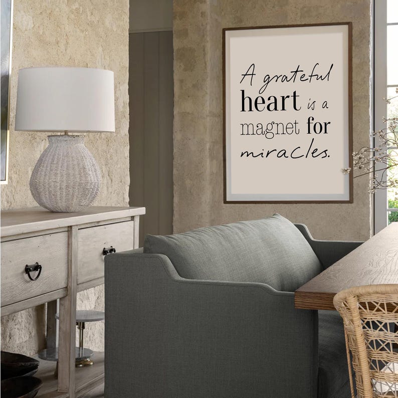Pu&ograve; includere: Interno di una stanza con una lampada bianca intrecciata su un mobile in legno chiaro. Una stampa incorniciata sulla parete mostra il testo "A grateful heart is a magnet for miracles." Sono visibili anche una poltrona grigia e una sedia in vimini.