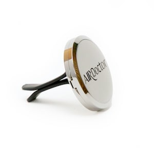 May include: A silver car air freshener with the text "AIRDoctor" in black script. The air freshener has a circular design with a silver finish and black vent clips.