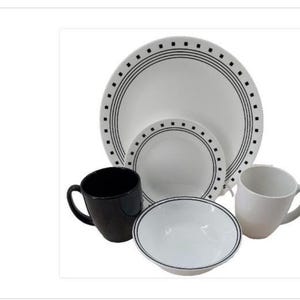 Puede incluir: Un juego de vajilla blanco con detalles en negro. El juego incluye platos, cuencos y tazas. Los platos tienen un borde negro punteado y líneas concéntricas negras. Una taza es negra, la otra blanca.