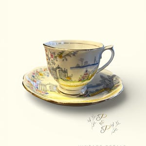 Peut inclure: Un ensemble tasse et soucoupe en porcelaine blanche orné d'une scène de jardin peinte à la main avec des portails en fer forgé, des fleurs colorées et de la verdure. Le bord de la tasse et de la soucoupe est souligné d'un fin liseré doré.