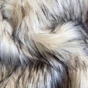May include: Close-up of faux fur fabric with a mix of cream, black, and gray fibers. The texture is dense and fluffy, with long, soft strands creating a luxurious appearance. The color palette is neutral, with a subtle sheen.