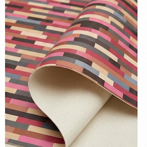 May include: A roll of patterned fabric with a geometric design. The pattern features rectangular shapes in pink, red, brown, grey, and beige. The fabric is partially rolled, revealing a beige canvas backing.
