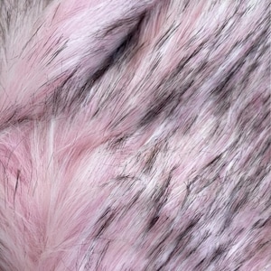 May include: Close-up of a faux fur fabric with a blend of pink, white, and black fibers. The texture is soft and fluffy, with long, flowing strands creating a luxurious appearance. The color palette is predominantly pastel pink.