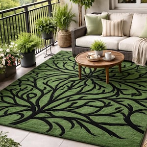 Puede incluir: Alfombra verde para exteriores con diseño de ramas de árbol negras. La alfombra rectangular está colocada en un patio embaldosado. El patio tiene una barandilla de metal negro, un sofá de mimbre con cojines crema y varias plantas en macetas.