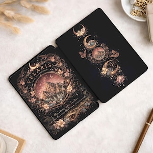 May include: Two black tablet cases with celestial designs. One features the text "VELARIS CITY OF STARLIGHT" and a mountain scene within a floral wreath. The other displays moon phases, butterflies, and floral accents in gold and pink.