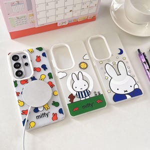 Op de afbeelding: Drie transparante telefoonhoesjes met verschillende ontwerpen. Eén hoesje heeft een patroon van kleurrijke konijnenvormen, een ander heeft een cartoonkonijn met een zon en wolken, en de derde heeft een konijn met sterren en een maan. Het woord "miffy" staat op twee van de hoesjes.