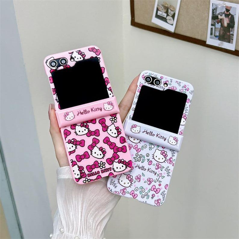 May include: Two phone cases with a Hello Kitty design. One case is pink with a pattern of Hello Kitty faces and bows. The other case is white with a floral and Hello Kitty pattern. Both cases have the words "Hello Kitty" printed on them.