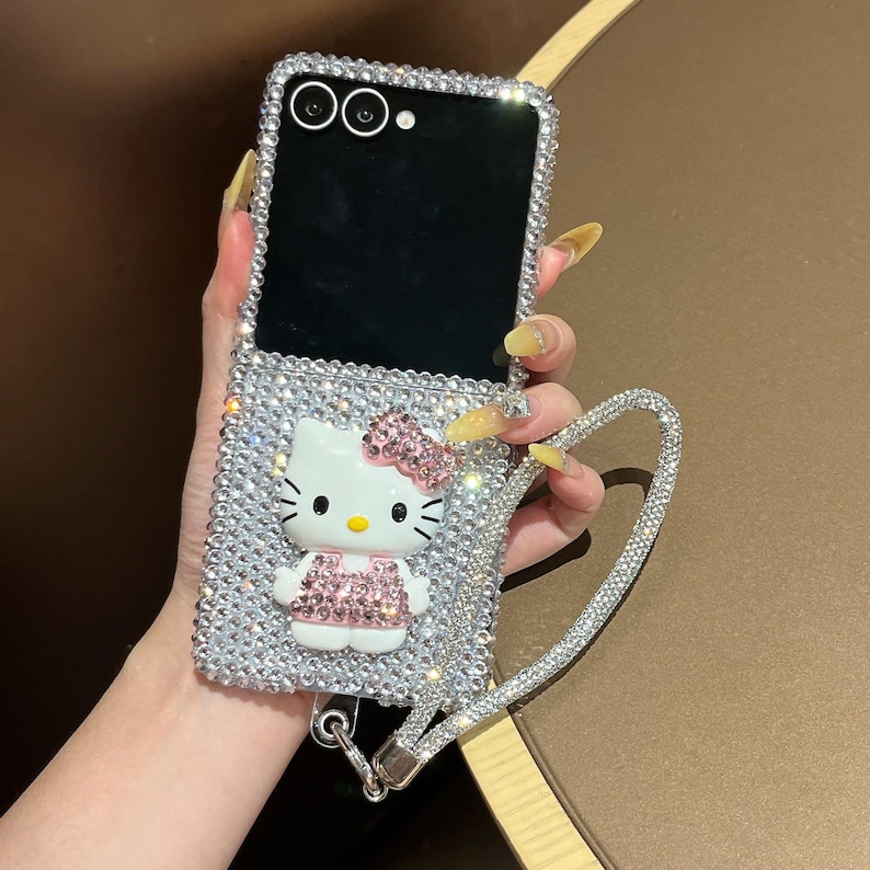 Puede incluir: Funda de tel&eacute;fono plateada cubierta de pedrer&iacute;a con un dise&ntilde;o de Hello Kitty con lazo y vestido rosa. La funda tiene una correa de mu&ntilde;eca de pedrer&iacute;a a juego. La funda est&aacute; dise&ntilde;ada para un tel&eacute;fono plegable.