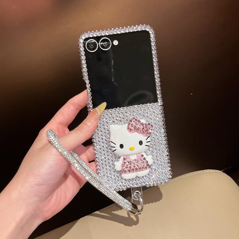Puede incluir: Funda de tel&eacute;fono adornada con pedrer&iacute;a con un dise&ntilde;o de Hello Kitty. La funda est&aacute; cubierta de pedrer&iacute;a plateada y presenta una figura 3D de Hello Kitty con un lazo y un vestido rosas. Se adjunta una correa de mu&ntilde;eca de pedrer&iacute;a a juego.