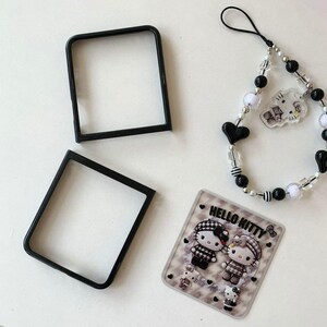 May include: An assortment of accessories including two black square frames, a beaded charm bracelet with black and white beads, and a Hello Kitty graphic. The Hello Kitty graphic features two cartoon characters and the text "HELLO KITTY".