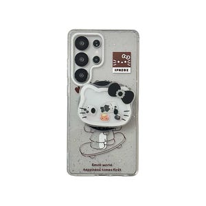 Puede incluir: Una funda transparente para tel&eacute;fono con un fondo brillante que presenta un dise&ntilde;o de Hello Kitty blanco sobre una patineta. El dise&ntilde;o incluye un lazo negro y el texto "Small world, happiness tomes first". La funda tambi&eacute;n tiene un peque&ntilde;o logotipo y el texto "IPHZOI".