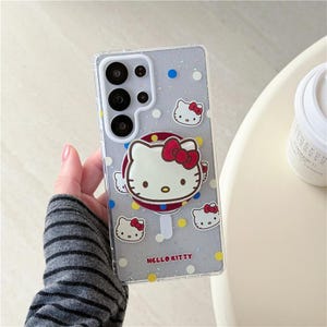 K&ouml;nnte beinhalten: Transparente Handyh&uuml;lle mit Hello Kitty-Design. Die H&uuml;lle zeigt ein gro&szlig;es Hello Kitty-Gesicht mit roter Schleife, umgeben von kleineren Hello Kitty-Gesichtern und Punkten. Die Worte "Hello Kitty" sind unten aufgedruckt.