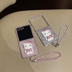 Puede incluir: Dos fundas de tel&eacute;fono adornadas con brillantes, una abierta y otra cerrada, con una combinaci&oacute;n de colores rosa y plata. Cada funda tiene un dise&ntilde;o 3D de Hello Kitty y una correa de mu&ntilde;eca a juego. Las fundas est&aacute;n cubiertas de peque&ntilde;os brillantes.