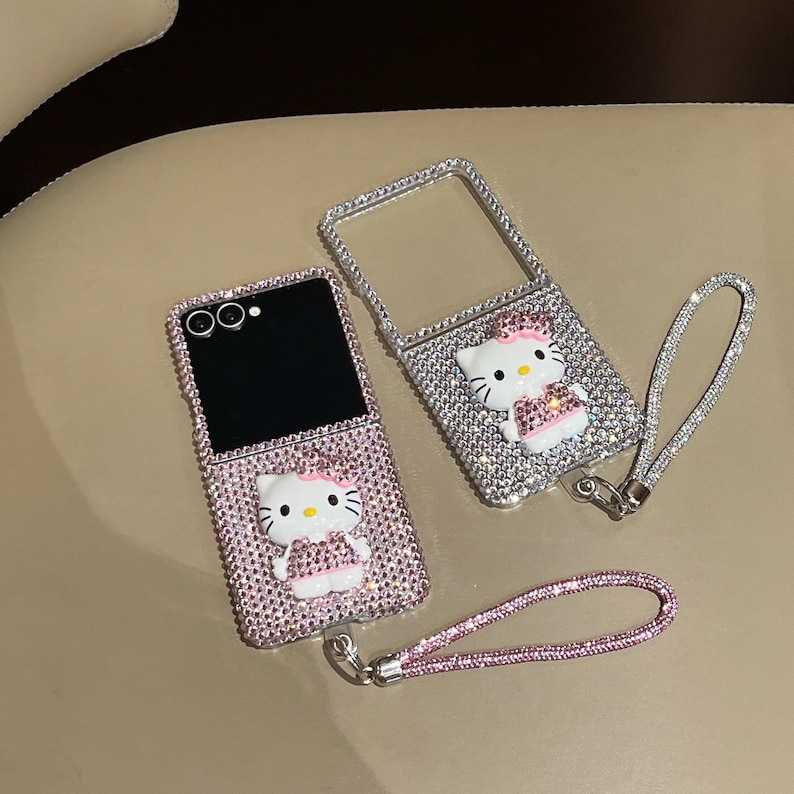 Puede incluir: Dos fundas de tel&eacute;fono adornadas con brillantes, una abierta y otra cerrada, con una combinaci&oacute;n de colores rosa y plata. Cada funda tiene un dise&ntilde;o 3D de Hello Kitty y una correa de mu&ntilde;eca a juego. Las fundas est&aacute;n cubiertas de peque&ntilde;os brillantes.