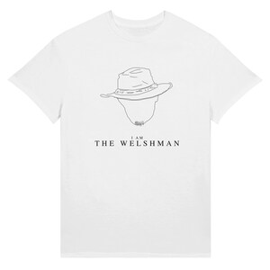 May include: White t-shirt featuring a minimalist line drawing of a hat and a silhouette of a face. Below the image is the text "I AM THE WELSHMAN" in a simple, sans-serif font. The shirt is made of a soft, opaque material.