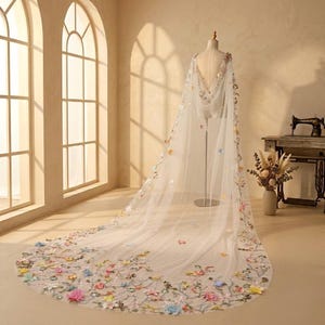 Könnte beinhalten: Ein bodenlanger, transparenter Umhang aus weißem Tüll mit einem komplexen, mehrfarbigen Blumenstickmuster. Das Design umfasst zarte Ranken und verschiedene Blüten in Rosa-, Blau-, Gelb- und Grüntönen, die den Rücken hinunterfließen.
