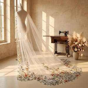 May include: A flowing, sheer white bridal veil with floral embroidery in shades of yellow, orange, and green. The veil is draped over a mannequin, showcasing its length and delicate design. The background includes a vintage sewing machine and a vase of flowers.