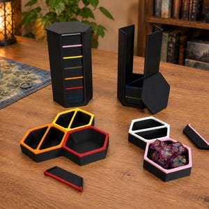Könnte beinhalten: Ein modulares, schwarzes, hexagonales Würfelaufbewahrungs- und Tablettsystem mit farbigen Akzenten in Pink, Gelb, Grün, Orange, Rot und Blau. Das Set enthält stapelbare sechseckige Behälter, einzelne Tablettsegmente und einen Deckel, wobei ein Tablett ein Set aus mehrfarbigen polyedrischen Würfeln enthält.