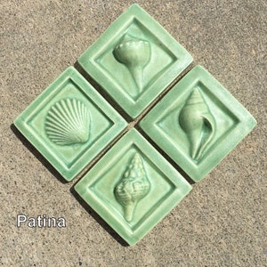 May include: Four green ceramic tiles with raised images of seashells. The tiles are arranged in a diamond pattern. The word "Patina" is written in white below the tiles.