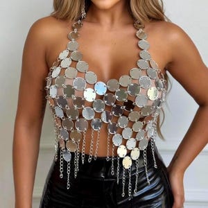 May include: A silver halter top made of connected circular metal pieces. The top features a plunging neckline and dangling chain fringe. The garment is designed to be worn as a top and is a statement piece.