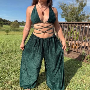 May include: A dark green two-piece set featuring a halter-style crop top with a central ring and crisscross waist ties, paired with matching wide-leg trousers. Both pieces are crafted from a textured fabric with a tonal leaf pattern design.