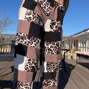May include: Patchwork trousers with a mix of leopard print, black, brown, and white fabric squares. The trousers have a wide-leg design and a high waist. The trousers are made of a soft material.