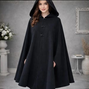 May include: A black hooded cape with a toggle closure. The cape is made of a soft material and has a wide, flowing design. The hood is large and covers the head and shoulders. The cape is a versatile garment for various occasions.